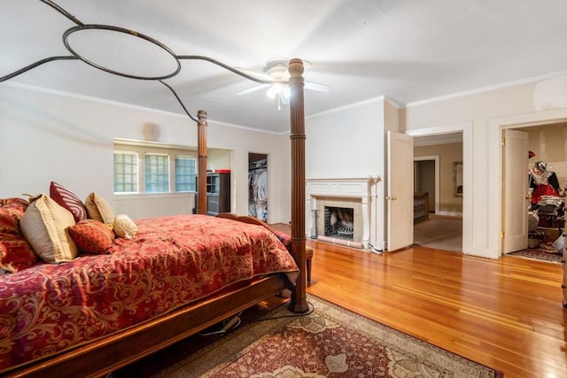 bedroom with a closet, hardwood / wood-style flooring, ceiling fan, ornamental molding, and a tiled fireplace