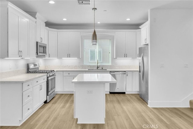 kitchen with appliances with stainless steel finishes, white cabinetry, sink, hanging light fixtures, and a center island