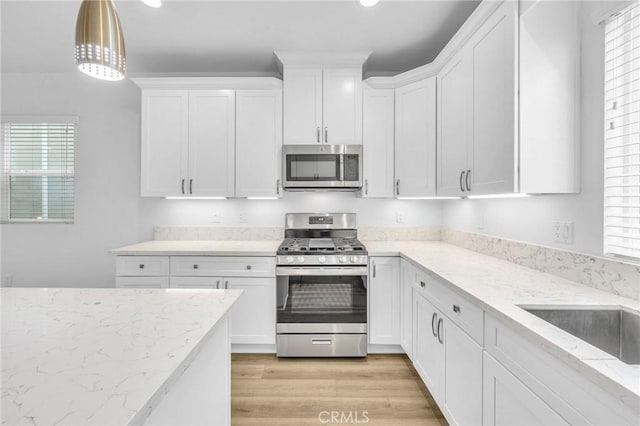 kitchen featuring white cabinetry, appliances with stainless steel finishes, light stone counters, and decorative light fixtures