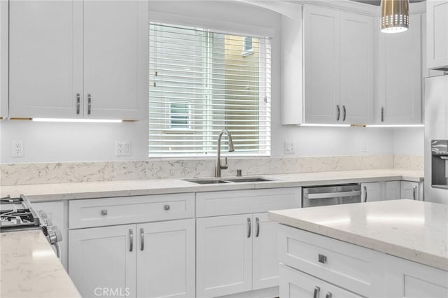 kitchen with sink, appliances with stainless steel finishes, white cabinetry, hanging light fixtures, and light stone counters