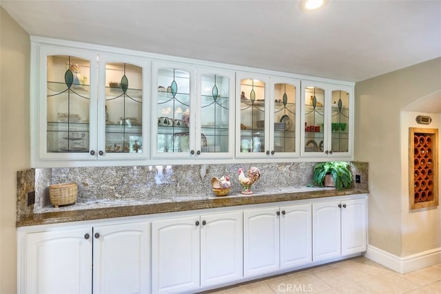 bar featuring decorative backsplash, light tile patterned floors, baseboards, and arched walkways