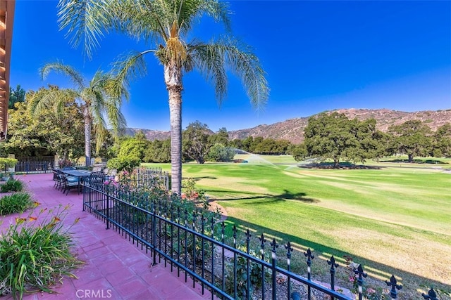 view of community with a patio, golf course view, fence, a yard, and a mountain view