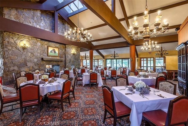 dining room featuring beam ceiling, high vaulted ceiling, a notable chandelier, a skylight, and a fireplace