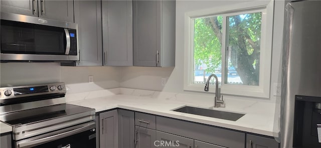 kitchen featuring gray cabinetry, light stone countertops, appliances with stainless steel finishes, and sink