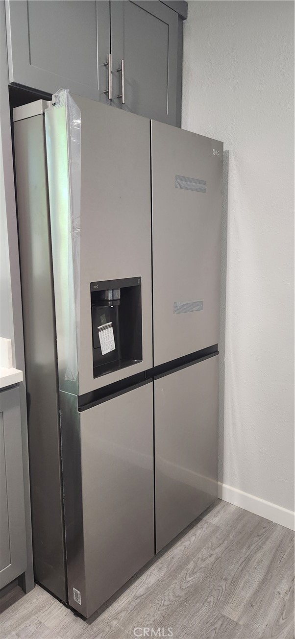 interior details with light hardwood / wood-style floors, gray cabinetry, and stainless steel fridge with ice dispenser