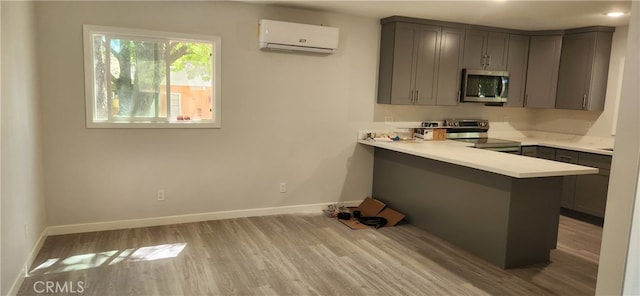 kitchen featuring appliances with stainless steel finishes, a wall mounted air conditioner, kitchen peninsula, a kitchen breakfast bar, and light hardwood / wood-style floors