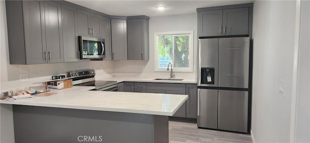 kitchen featuring kitchen peninsula, light wood-type flooring, sink, gray cabinetry, and stainless steel appliances