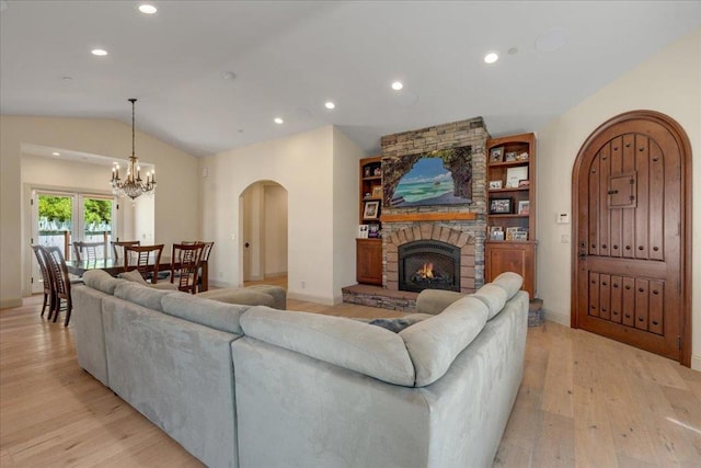 living room with a stone fireplace, light hardwood / wood-style flooring, an inviting chandelier, and vaulted ceiling