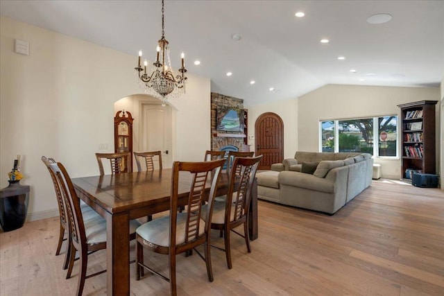 dining space with a stone fireplace, lofted ceiling, light hardwood / wood-style flooring, and an inviting chandelier