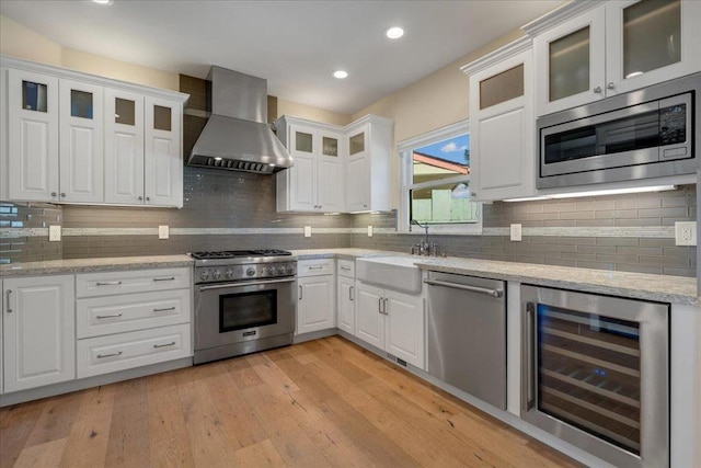 kitchen featuring wall chimney exhaust hood, stainless steel appliances, beverage cooler, white cabinets, and light hardwood / wood-style floors