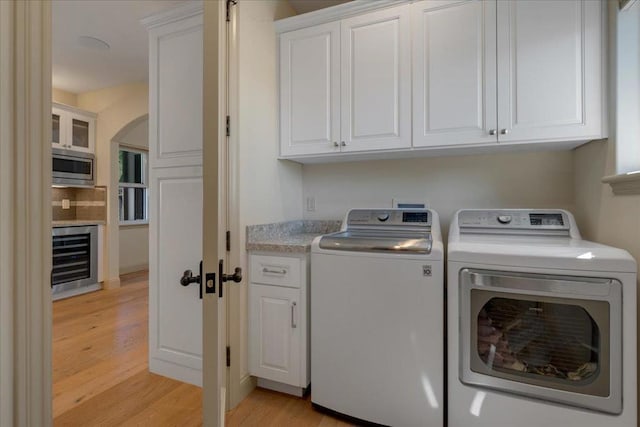 clothes washing area with cabinets, wine cooler, light wood-type flooring, and washer and dryer