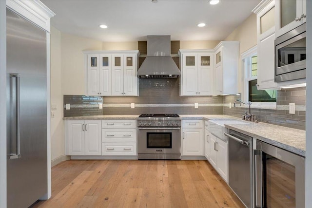 kitchen featuring wall chimney range hood, white cabinetry, beverage cooler, built in appliances, and light hardwood / wood-style flooring