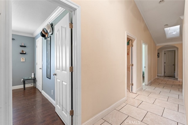 hall with light wood-type flooring, crown molding, and lofted ceiling with skylight