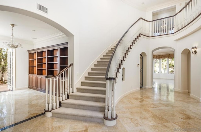 staircase with an inviting chandelier, a towering ceiling, and crown molding