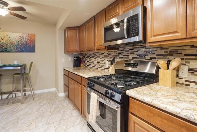 kitchen featuring light stone counters, backsplash, stainless steel appliances, and ceiling fan