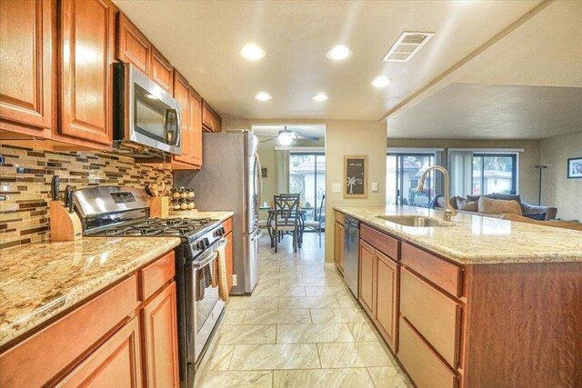 kitchen with ceiling fan, sink, a kitchen island with sink, light stone countertops, and stainless steel appliances