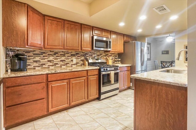 kitchen featuring stainless steel appliances, sink, backsplash, ceiling fan, and light stone counters