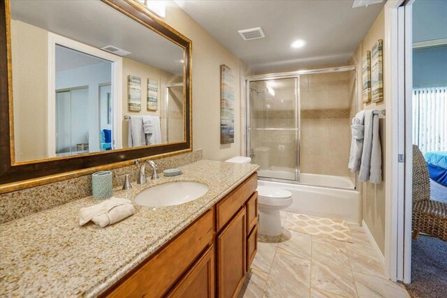 full bathroom with combined bath / shower with glass door, vanity, and toilet