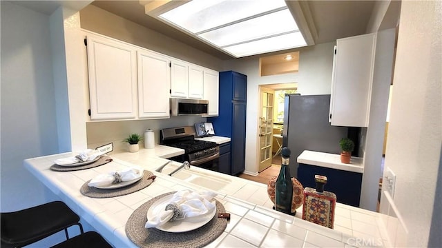 kitchen featuring tile countertops, blue cabinets, sink, appliances with stainless steel finishes, and white cabinetry