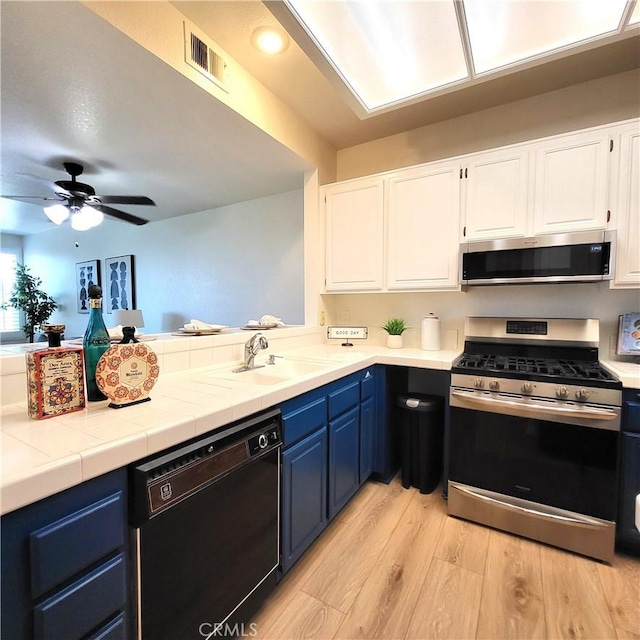 kitchen with sink, blue cabinetry, appliances with stainless steel finishes, light hardwood / wood-style floors, and white cabinetry