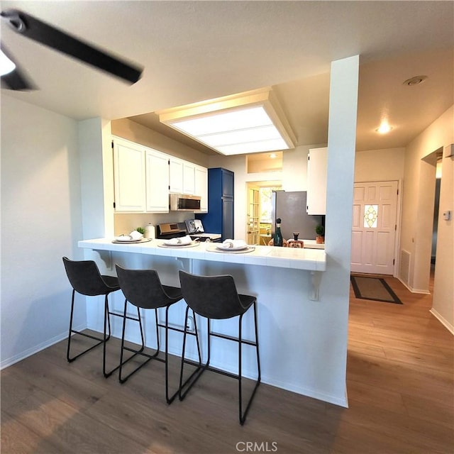 kitchen with a breakfast bar, dark wood-type flooring, white cabinetry, kitchen peninsula, and stainless steel appliances