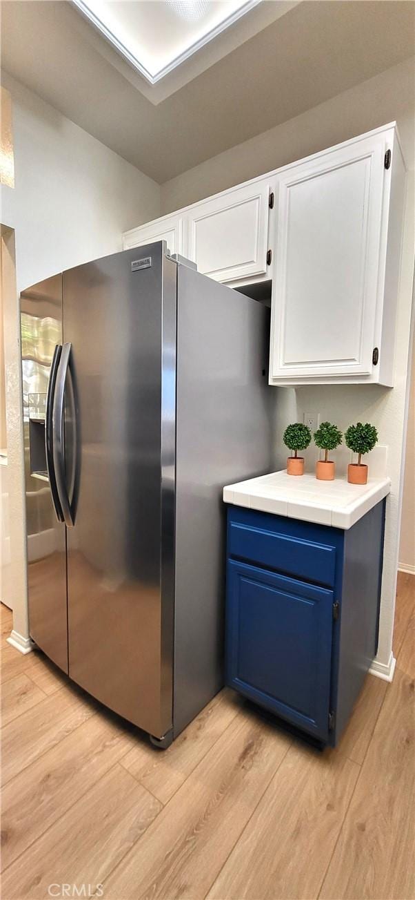 kitchen featuring stainless steel fridge with ice dispenser, white cabinetry, blue cabinets, and light hardwood / wood-style flooring