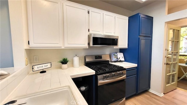 kitchen with stainless steel appliances, white cabinetry, and blue cabinets