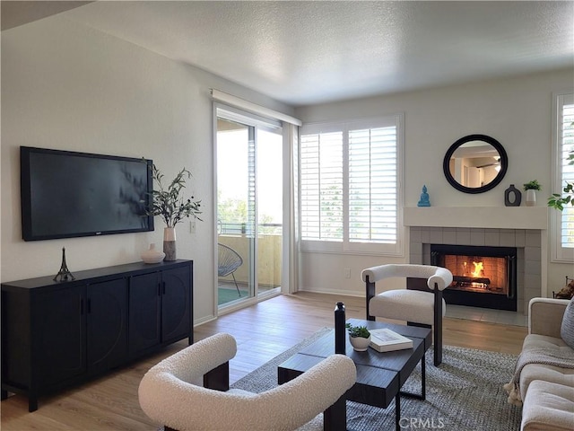 living room with light hardwood / wood-style floors, a textured ceiling, and a tiled fireplace