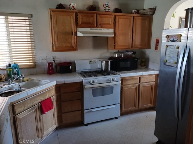 kitchen featuring white gas range, tile counters, sink, and stainless steel fridge