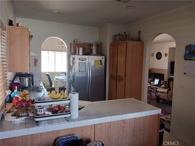 kitchen with stainless steel refrigerator, kitchen peninsula, and tile countertops