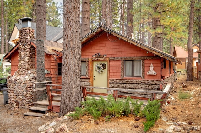 view of front of home featuring a shingled roof, stone siding, and a chimney