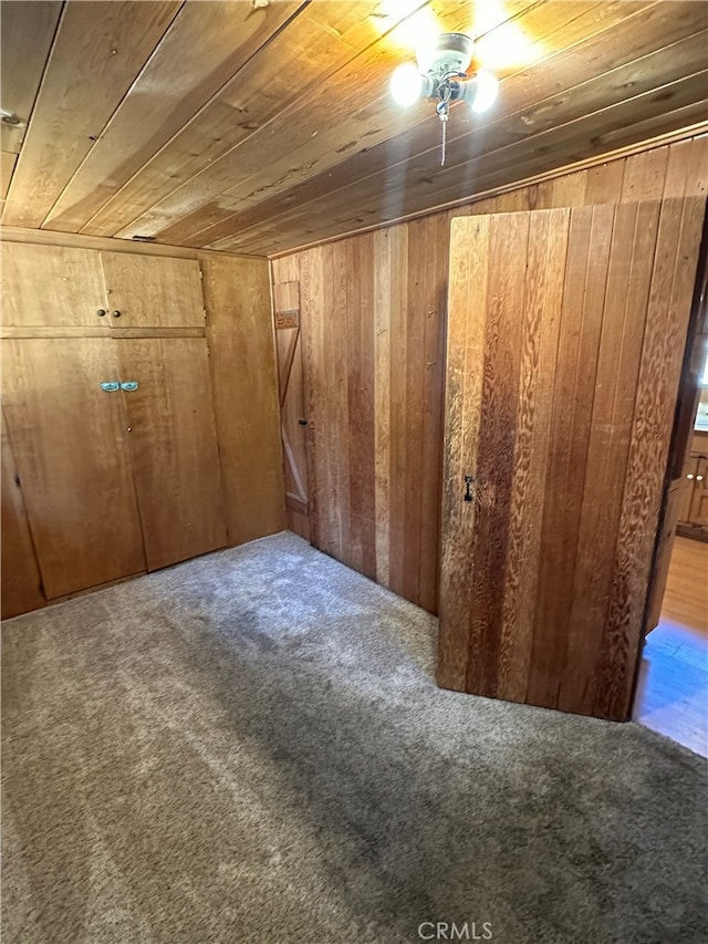 interior space with wood ceiling, wood walls, ceiling fan, and light colored carpet