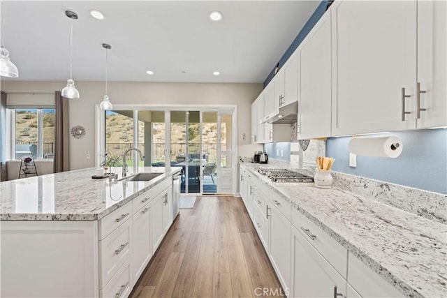 kitchen with white cabinets, sink, hanging light fixtures, stainless steel gas cooktop, and a center island with sink