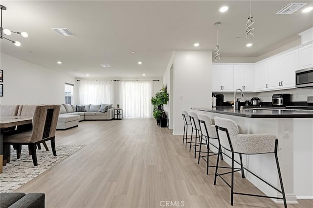 kitchen with a breakfast bar, decorative light fixtures, white cabinets, range, and light hardwood / wood-style floors