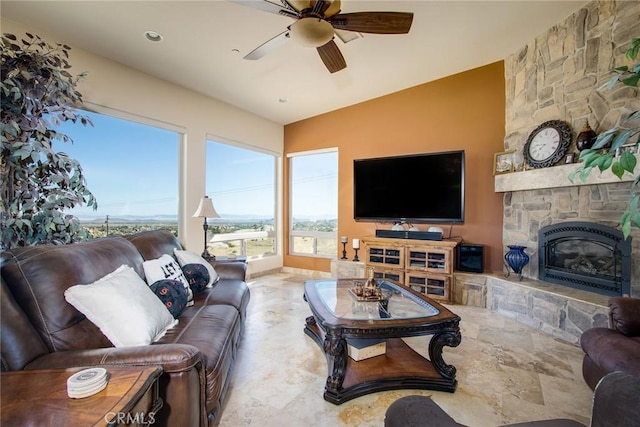 living room with vaulted ceiling, a ceiling fan, and a stone fireplace