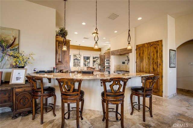 kitchen with light stone countertops, double oven, a kitchen bar, and hanging light fixtures