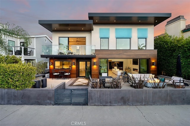 back house at dusk featuring outdoor lounge area, a balcony, and a patio area