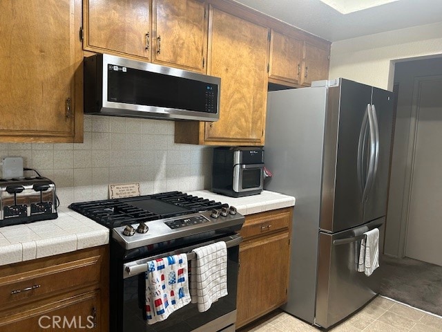 kitchen with decorative backsplash, light tile patterned floors, stainless steel appliances, and tile countertops