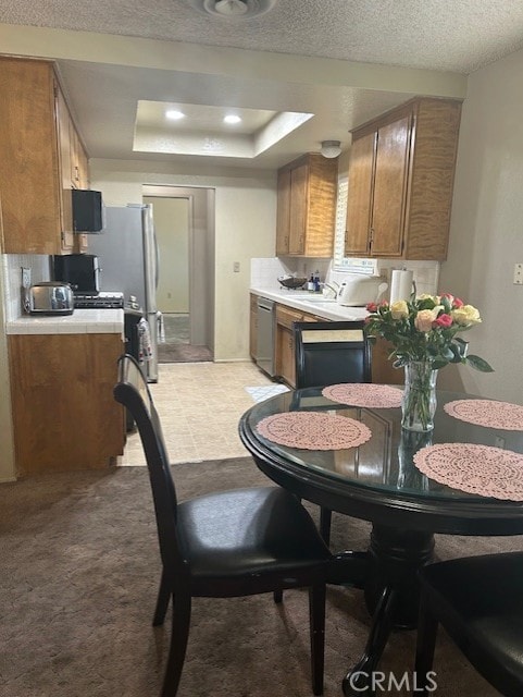 kitchen with a raised ceiling, kitchen peninsula, a textured ceiling, stainless steel dishwasher, and light colored carpet