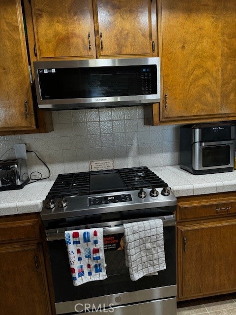 kitchen with appliances with stainless steel finishes, tile countertops, and tasteful backsplash