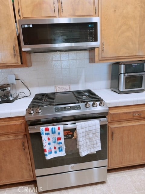 kitchen featuring appliances with stainless steel finishes, tile counters, backsplash, and light tile patterned floors