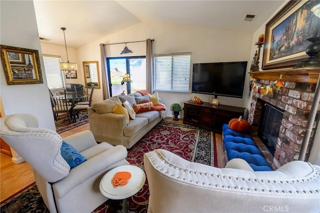 living room featuring a brick fireplace, hardwood / wood-style flooring, vaulted ceiling, and a notable chandelier