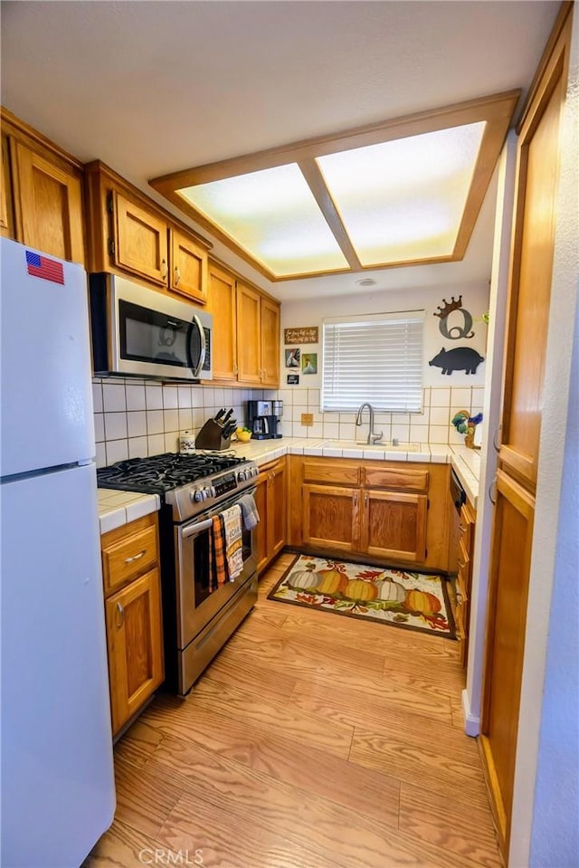 kitchen with tile countertops, backsplash, sink, light hardwood / wood-style flooring, and stainless steel appliances