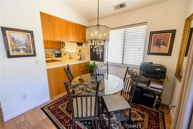 dining space with light hardwood / wood-style flooring, a chandelier, and vaulted ceiling