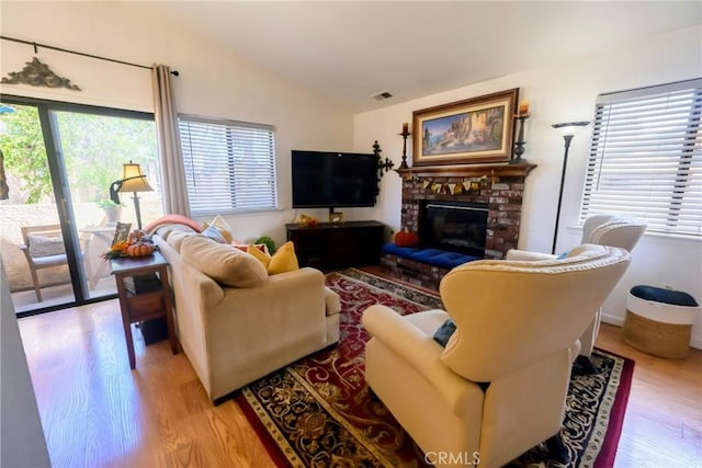 living room with a wealth of natural light, light hardwood / wood-style flooring, and a brick fireplace