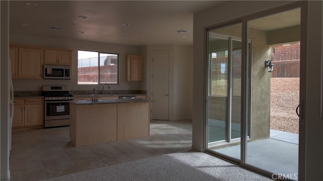 kitchen featuring appliances with stainless steel finishes, a kitchen island with sink, light brown cabinets, and light colored carpet