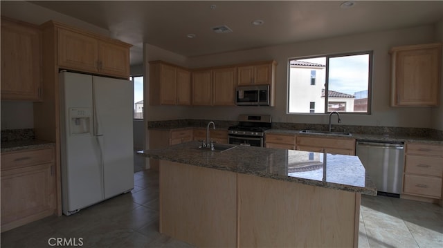 kitchen with an island with sink, appliances with stainless steel finishes, stone counters, and sink