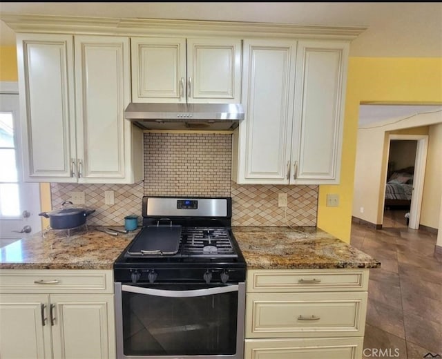 kitchen featuring stainless steel gas stove, cream cabinets, stone countertops, and backsplash