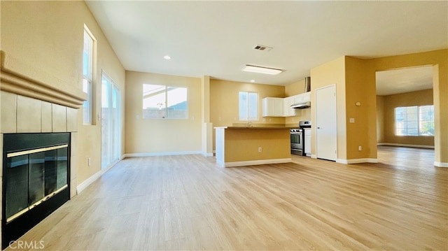 unfurnished living room with light wood-type flooring, a tiled fireplace, and sink