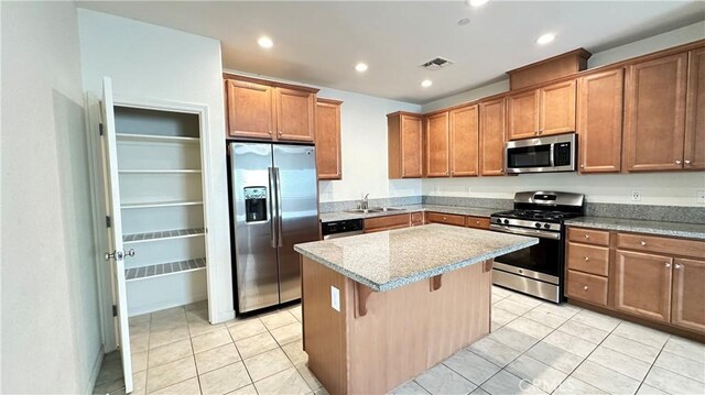 kitchen featuring a kitchen island, sink, a breakfast bar area, stainless steel appliances, and light stone countertops